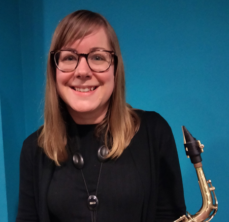 A Caucasian woman with mid length brown hair and glasses holding a saxophone